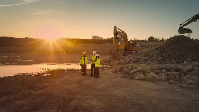 Aerial Drone Shot Of Construction Site With Excavators On Sunny Day: Diverse Team of Real Estate Developers Discussing Project. Civil Engineer, Architect, Inspector Talking And Using Tablet Computer.