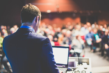 Speaker giving a talk on corporate business conference. Unrecognizable people in audience at...