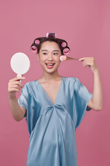 Cute girl with hair curlers doing makeup on her face at the makeup table, using makeup brush