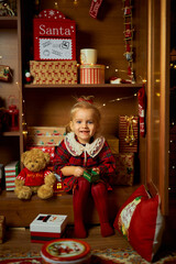 Merry Christmas and Happy Holiday. Cute little girl in a plaid dress sitting in the closet with gifts. Atmosphere of magic, enchantment and celebration