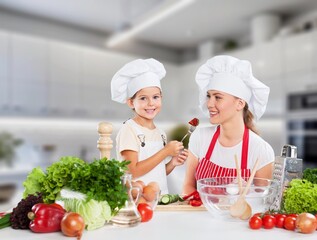 Attractive mother cooking with her cute daughter at home.