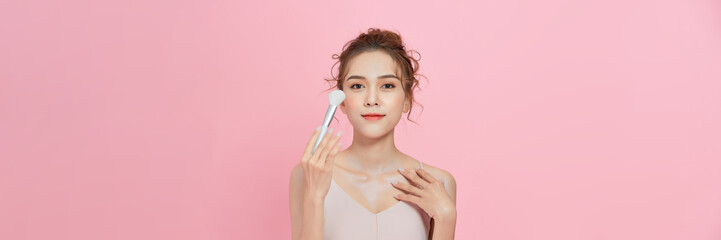Woman applies powder on the face using makeup brush.