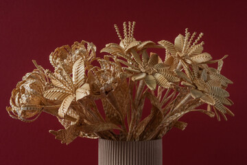 The flowers is made of straw on a red background in a cardboard vase
