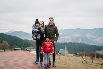 Family vacation with children in mountains. Mother, father embrace kids on terrace on an autumn...