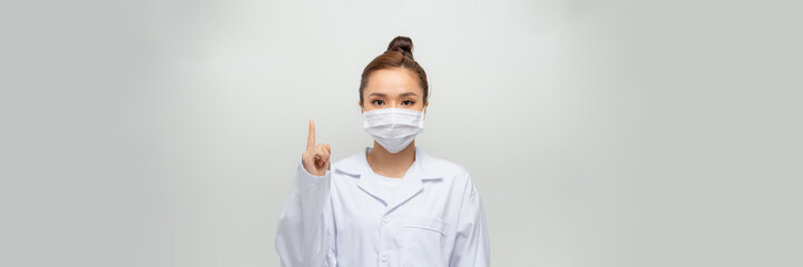 pretty, female doctor wearing a white overall raised a finger up as a sign of attention