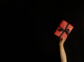 Hand holding red gift box with black ribbon over black background with free space for ads. Black Friday concept