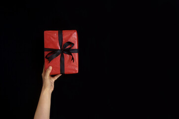 Hand holding red gift box with black ribbon on boxing day concept over black background with copy space