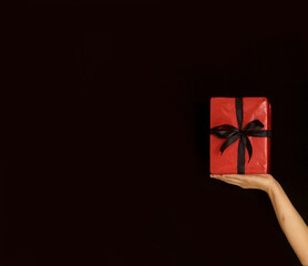 A red gift box with black ribbon on palm of female hand in Black Friday concept isolated over black background