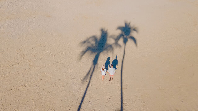 drone view from above at a couple of men and women walking on the beach with palm trees on the beach road of Pattaya Thailand, shadow of palm tree in the sand on the beach - Powered by Adobe