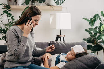 Worried young mommy calling to doctor because daughter coughing sneezing and having severe headache temperature at home. Unhealthy child with mother who distance remote talking with therapist indoors