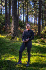 Adult woman standing in the forest, illuminated by sunlight. Active adult, hiking in Glendalough, Wicklow Mountains, Ireland