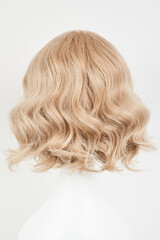 Naklejka premium Natural looking blonde fair wig on white mannequin head. Middle length hair cut on the plastic wig holder isolated on white background, back view