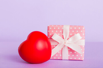 gift box with red bow and red heart on colored background. Perspective view. Flat lay