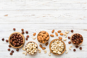 Fototapeta premium Assortment of nuts in wooden bowl on colored table. Cashew, hazelnuts, walnuts, almonds. Mix of nuts Top view with copy space