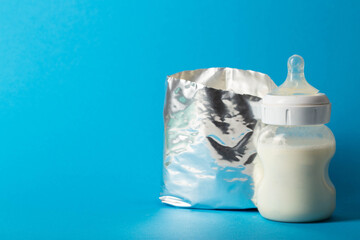 A shiny package with dry milk formula and a baby feeding bottle with milk on a blue background. Copy space for text, healthy microbiota