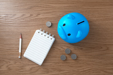 Piggy bank and coins and notebook on wooden texture background. Flat lay of a workplace. Accounting...