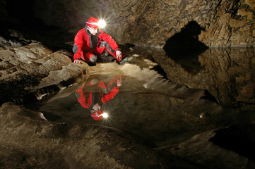 Reflection of a spelunker in a cave water pool. Acetylene gas lamp on helmet illuminating the...