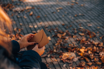A woman opens a brown envelope in an autumn park sitting on a bench