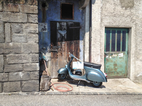 Brione sopra Minusio, Ticino, Switzerland - 02.18.2012: an old piaggo Vespa scooter stands in front of a wooden and green metal door of a building directly at the streets of Brione