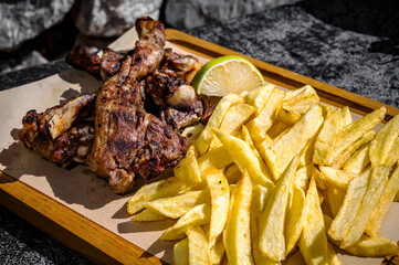 Grilled Lamb Spareribs on Wooden Board: Mouthwatering view of perfectly grilled lamb spareribs served on a rustic wooden board, accompanied by golden French fries. Selective focus