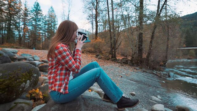 Photographer woman takes Polaroid photo along riverside among fall colors