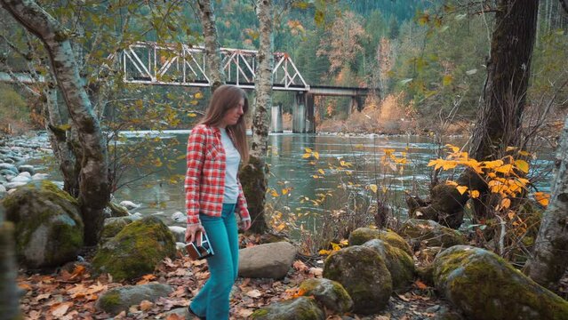 Photographer woman walks along riverside among fall colors and takes Polaroid