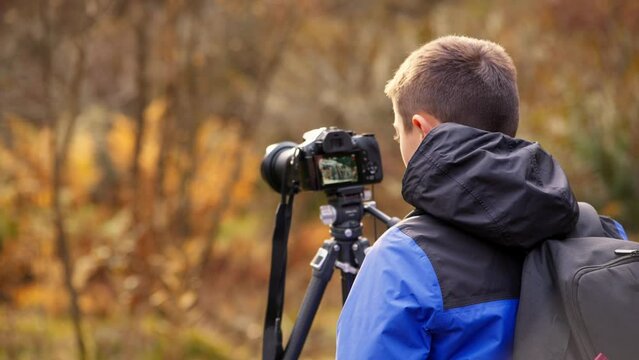 A young boy, camera in hand, photographs a tranquil autumn-winter woodland with a meandering stream. Exploring outdoor photography.