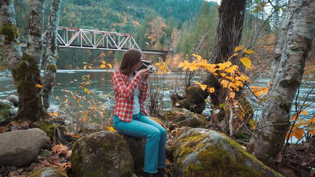 Photographer woman takes Polaroid photo along riverside among fall colors