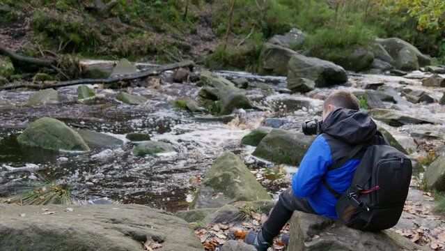 Young boy, camera and tripod, capturing serene autumn-winter woodland with a meandering stream. Enjoying outdoor photography.