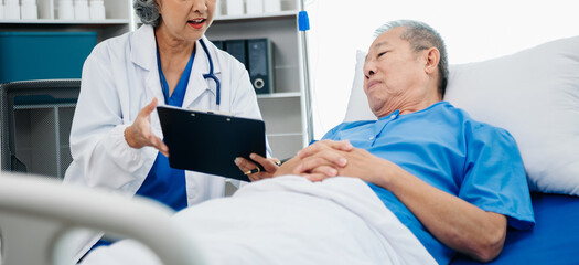 Obraz premium Asian doctor in white suit take notes while discussing and Asian elderly, man patient who lying on bed with receiving saline solution