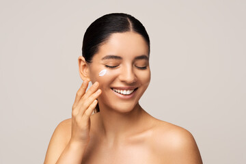 Seasonal face skin protection. Beauty shot of gorgeous multiracial woman with amazing smile applying cream on her face