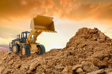Wheel loader are digging the soil in the construction site on the  sunset sky background .