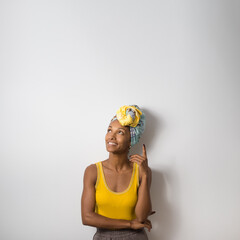 Portrait of beautiful happy young casual black woman wearing a headwrap looking and pointing up to blank space. - 677633037