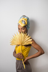 Portrait of beautiful happy young casual black woman wearing a headwrap and handing a yellow palm tree leaf. - 677633047