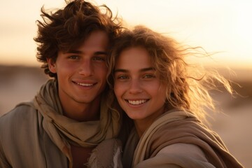Portrait of young couple in love embracing and looking at camera on the beach at sunset
