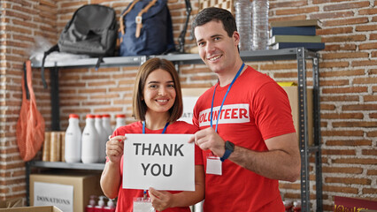 Man and woman volunteers standing together holding paper with thank you message at charity center