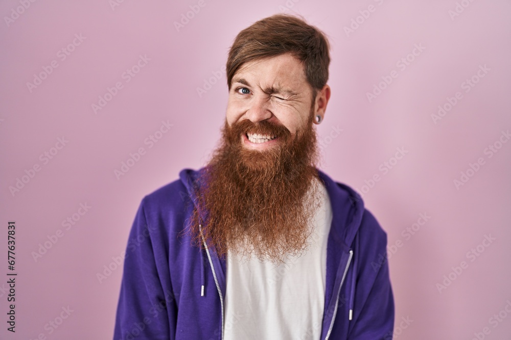 Canvas Prints Caucasian man with long beard standing over pink background winking looking at the camera with sexy expression, cheerful and happy face.