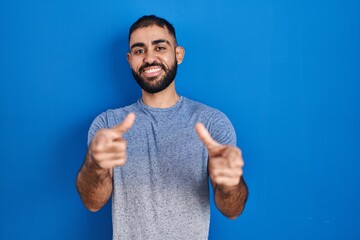 Middle east man with beard standing over blue background pointing fingers to camera with happy and...