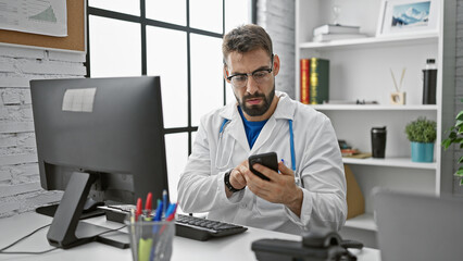 Handsome young hispanic man working as a doctor, engrossed in online consultation via smartphone at...