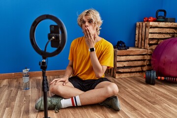 Young man recording training tutorial at the gym covering mouth with hand, shocked and afraid for...