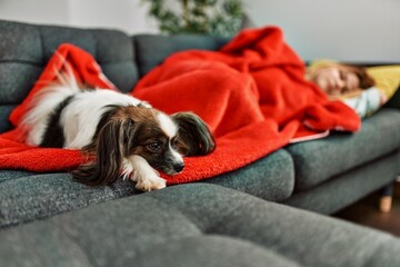 Young caucasian woman lying on sofa sleeping with dog at home