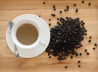 A white cup of Coffee place on the wooden plate with coffee beans scattered, angle from above. In the morning when the sun shines.