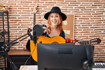 Fototapeta na wymiar Young caucasian woman playing classic guitar at music studio smiling happy pointing with hand and finger