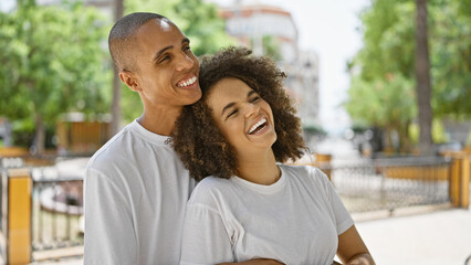 Beautiful couple, brimming with joy and laughter, standing confidently, hugging, and looking up at the sky in the park with smiles.