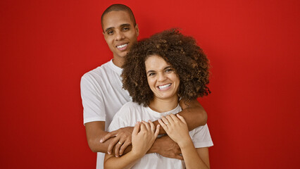 Beautiful couple expresses love through a confident hug, smiling joyfully over an isolated red background