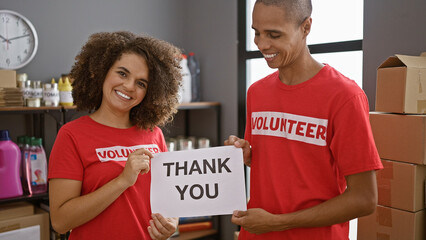 Two young activists, smiling man and woman volunteers holding a 'thank you' message at charity...