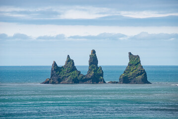 View of basalt stacks, pillars Reynisdrangar at black sand beach near Vik, South Iceland, summer, rainy blue sky.