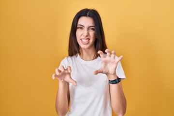 Young beautiful woman standing over yellow background smiling funny doing claw gesture as cat,...
