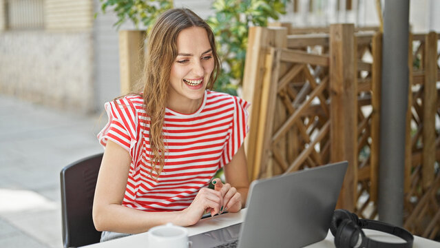 Young blonde woman using laptop sitting on table at coffee shop terrace