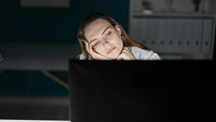 Young blonde woman doctor tired using computer working at clinic